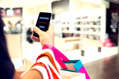 近景照片，男子手中拿著購物袋和手機，手機上有「網上購物」字樣。
