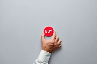 商人手握着一个印有「购买」字样的红色徽章，表示对现成公司的购买决策。